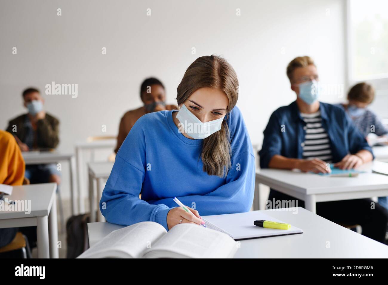 Young students with face masks at desks at college or university, coronavirus concept. Stock Photo