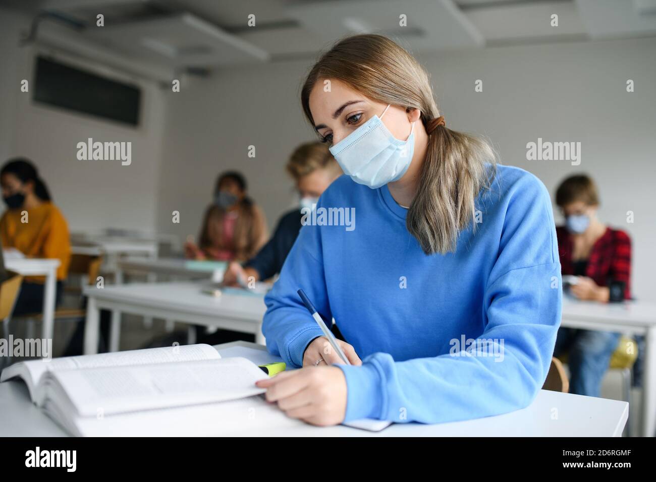 Young students with face masks at desks at college or university, coronavirus concept. Stock Photo