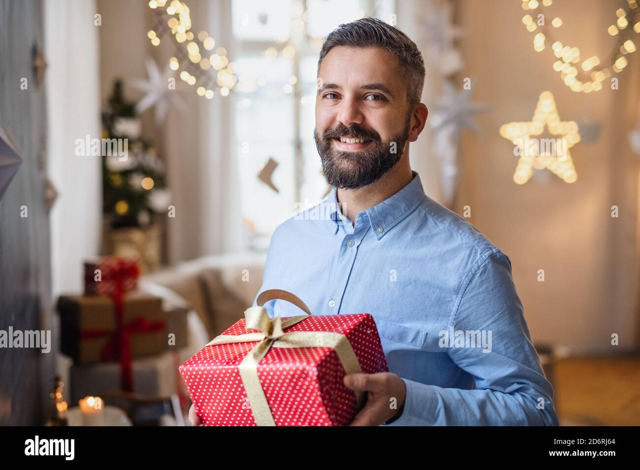 Mature man indoors at home at Christmas, holding present. Stock Photo