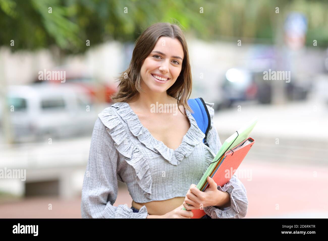 Happy student posing looking at camera with folders standing in the street Stock Photo