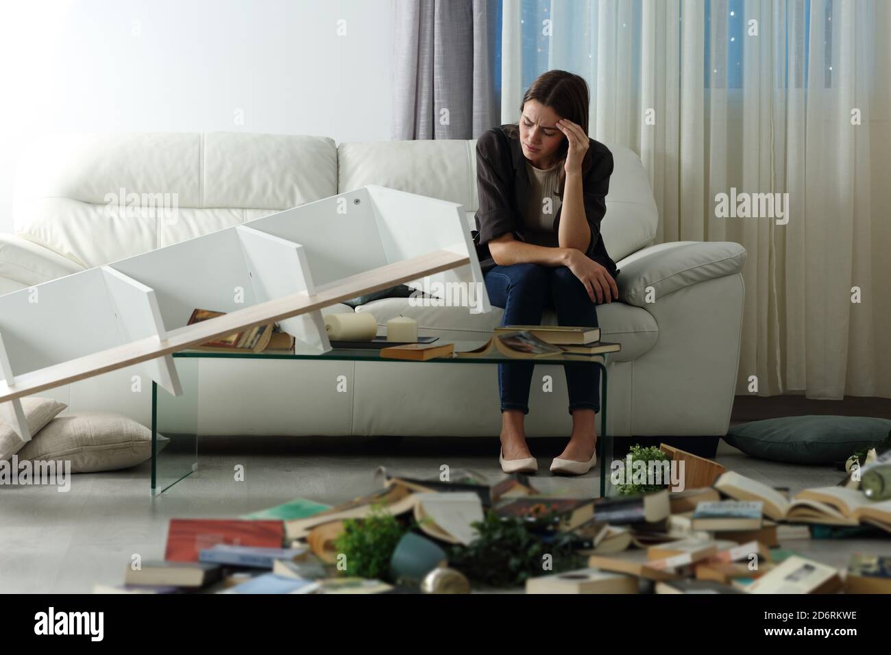 Sad tenant complaining after home robbery sitting on a couch in the night with messy living room Stock Photo