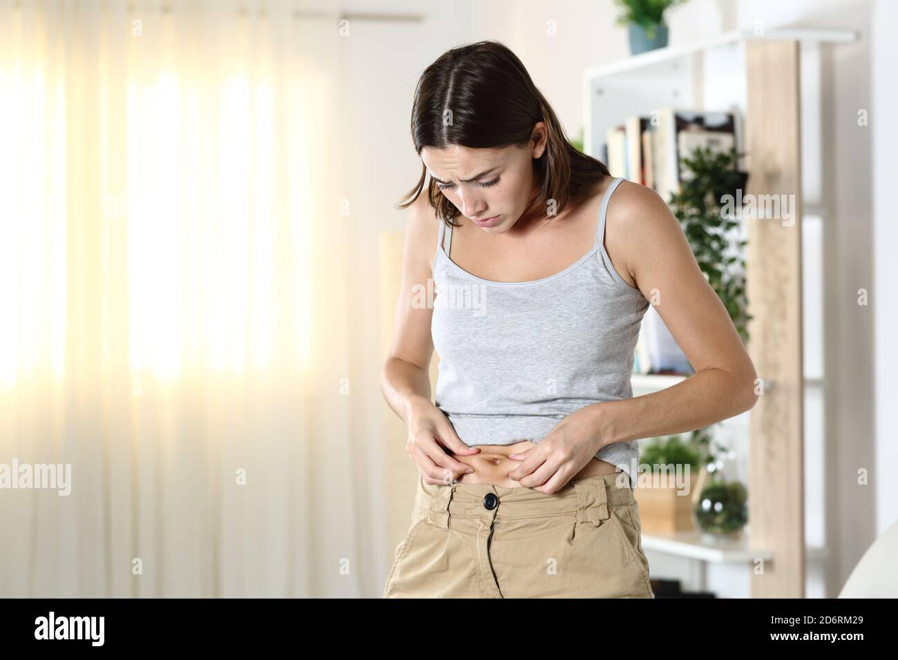 Woman worried about body fat touching her belly standing at home Stock Photo