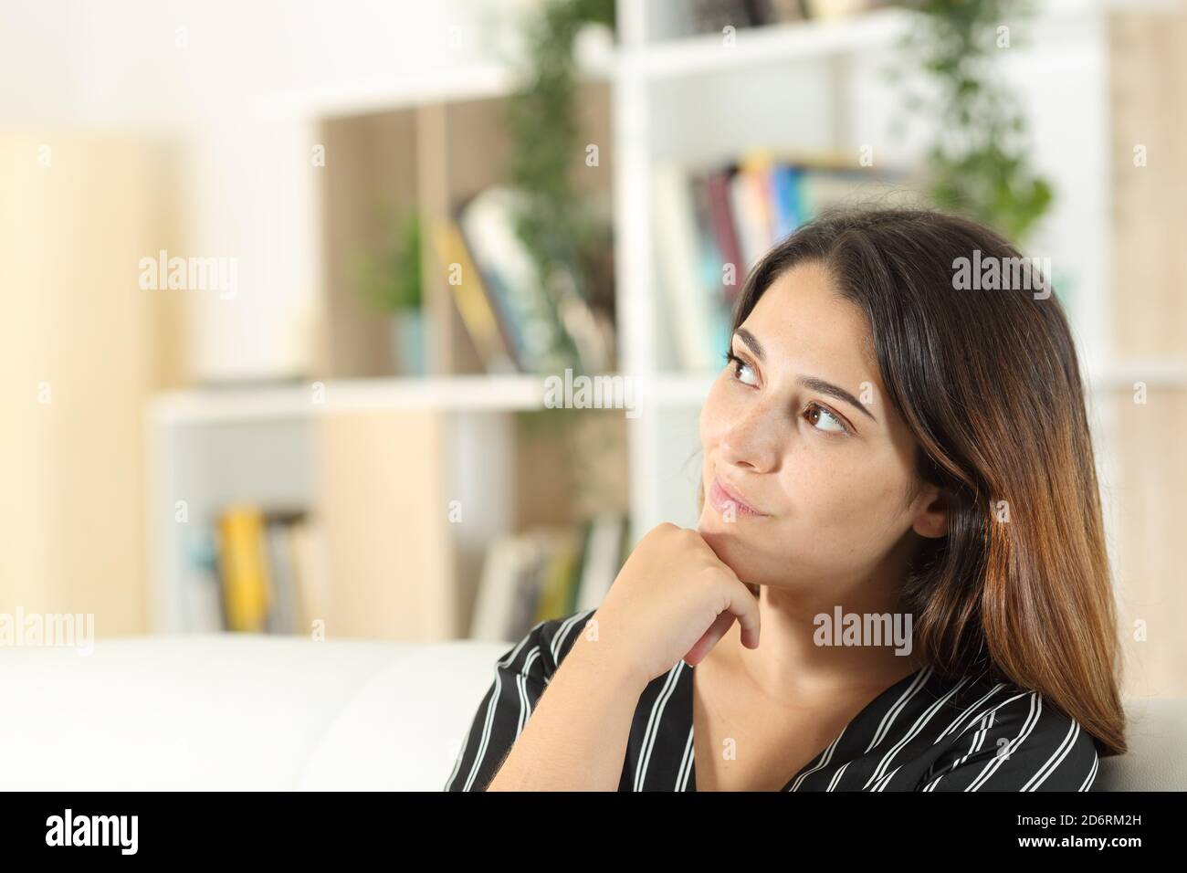 Thoughtful woman looking at side sitting on a sofa in the living room at home Stock Photo