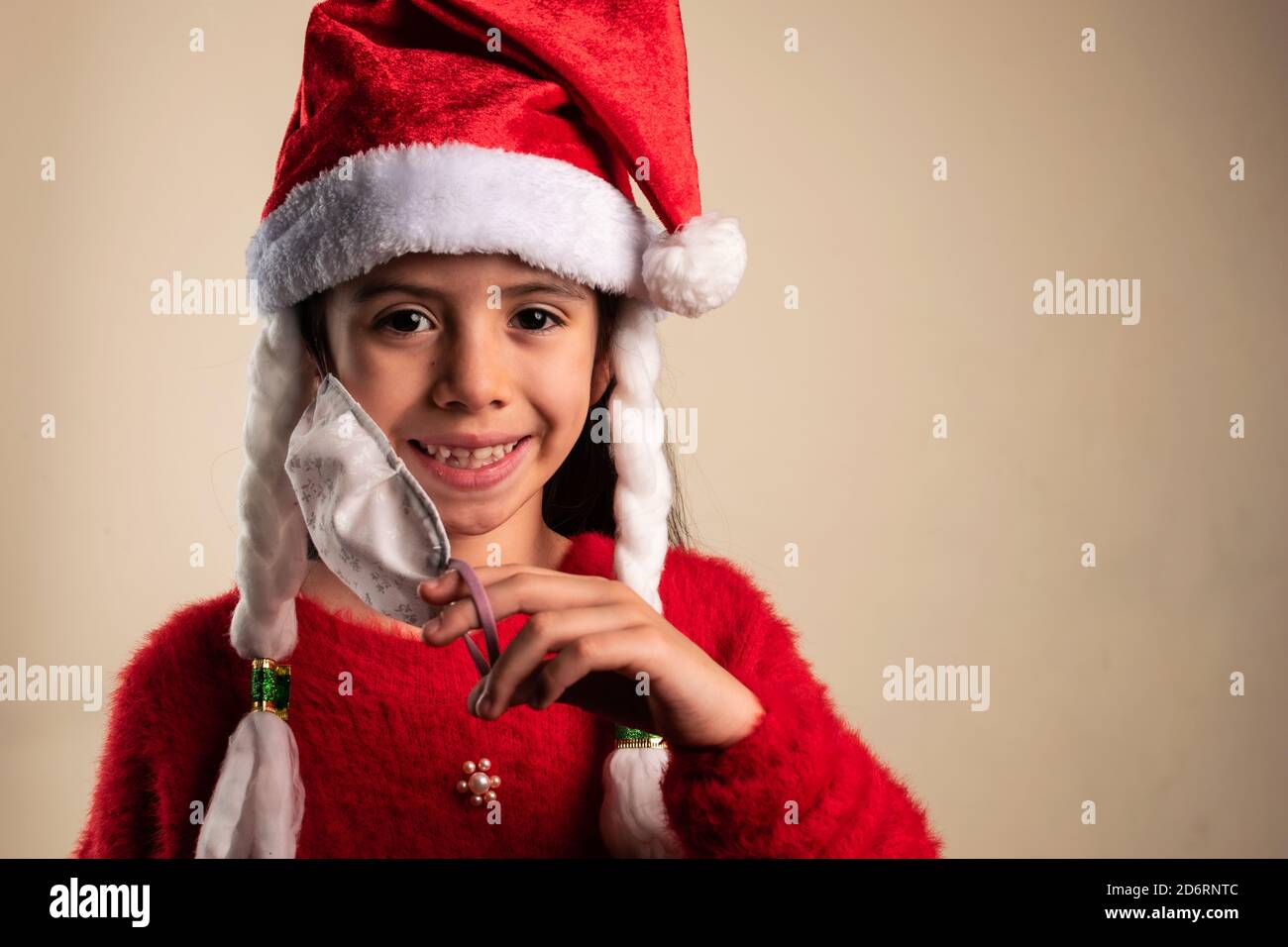 Girl wearing a red Santa Claus hat holding down her mask and smiling Stock Photo