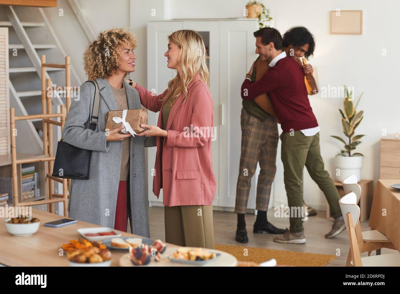 Group of elegant adult people greeting each other and exchanging gifts while welcoming guests at dinner party indoors Stock Photo