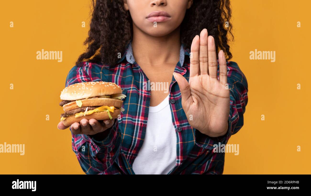 Black Lady Holding Burger And Showing Stop Gesture To Camera Stock Photo