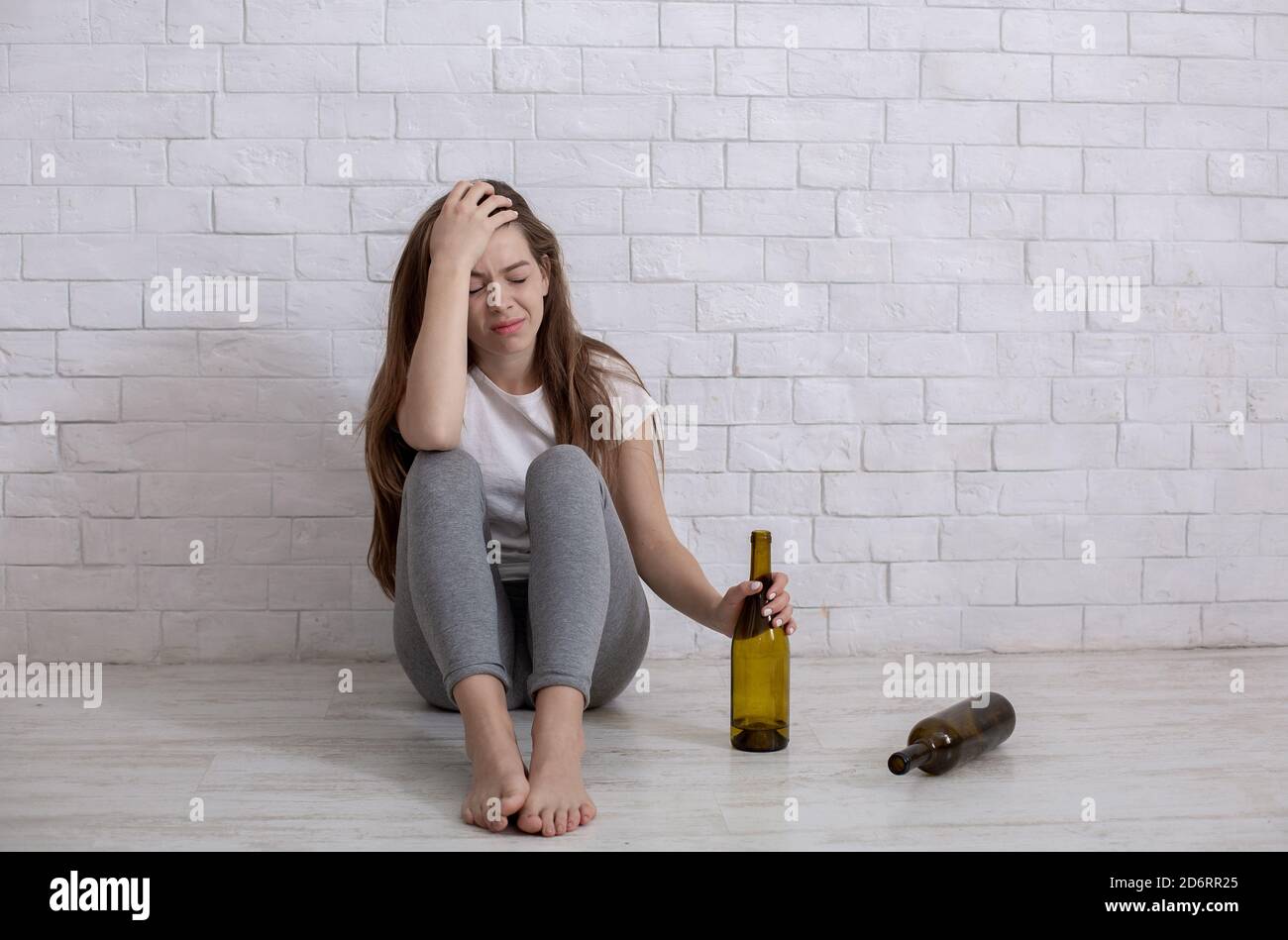 Alcohol abuse concept. Young depressed woman with bottle of booze sitting on floor at home, empty space Stock Photo
