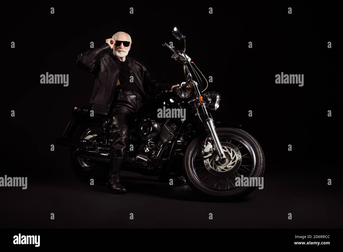 Full size photo of old man confident cool biker man sit bike touch sunglasses specs wear modern outfit isolated over black color background Stock Photo