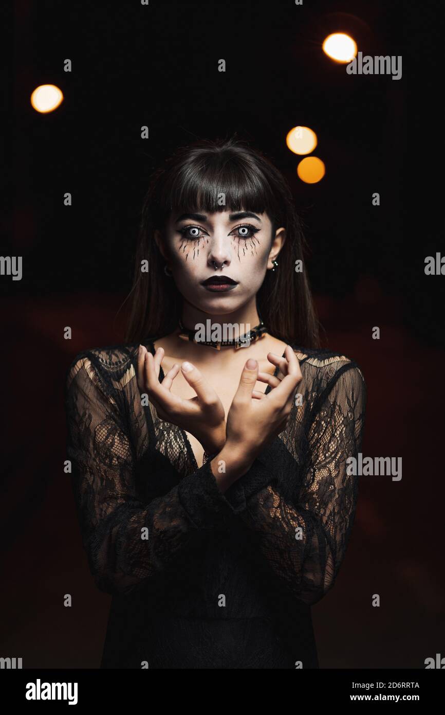 Unemotional female in black dress and with scary makeup standing in white  contact lenses on Halloween in darkness while looking at camera Stock Photo  - Alamy