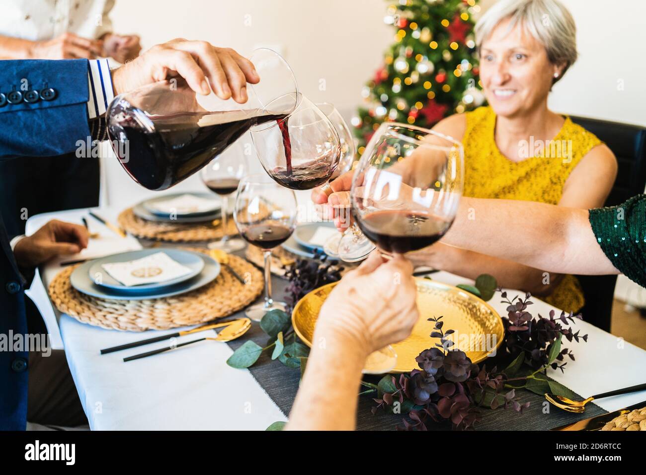 Cheerful friends and family members gathering together at table and holding glasses with red wine during Christmas dinner Stock Photo