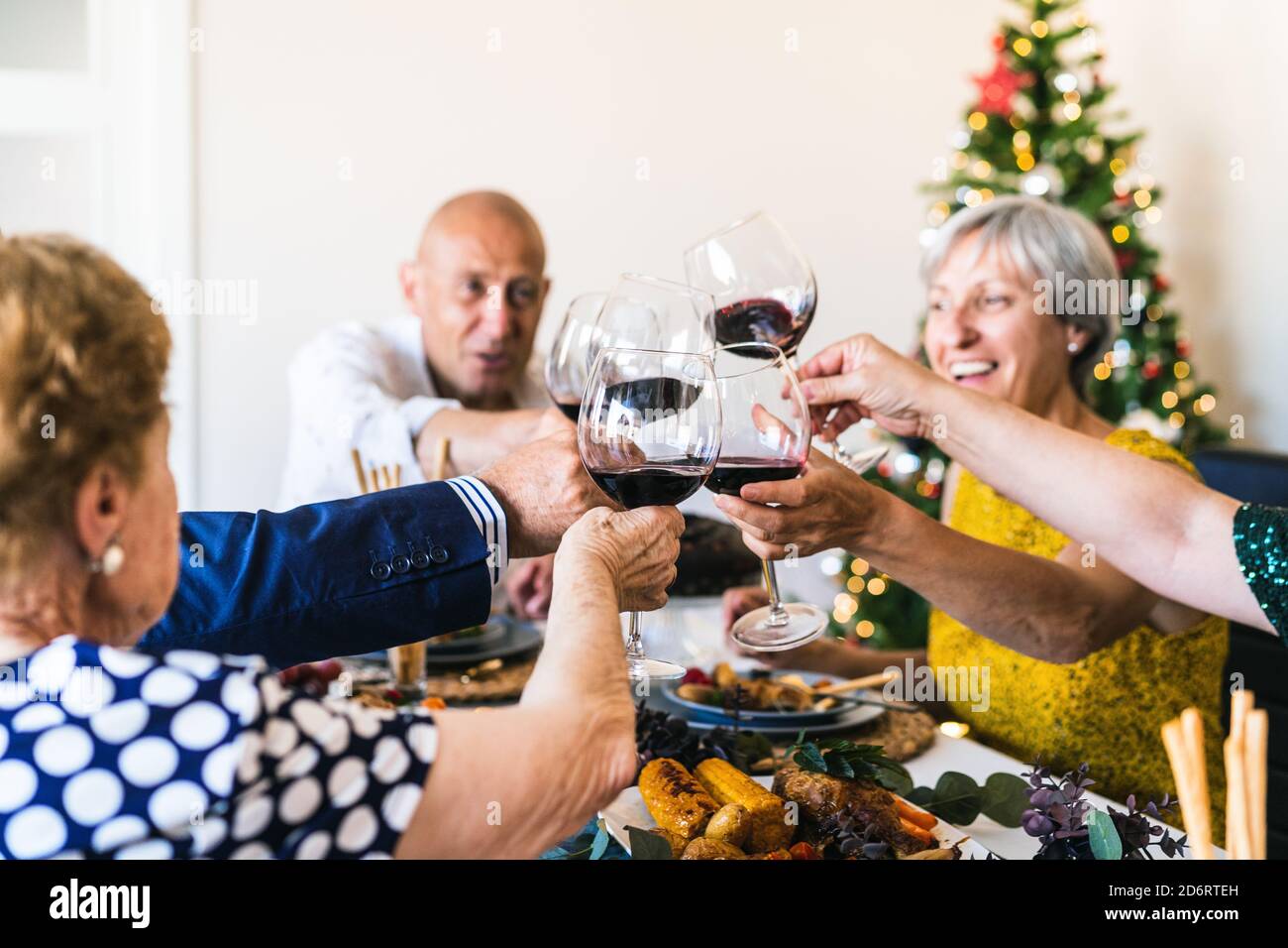 Happy partners raising glasses of alcoholic drink while gathering at table during festive event in apartment Stock Photo