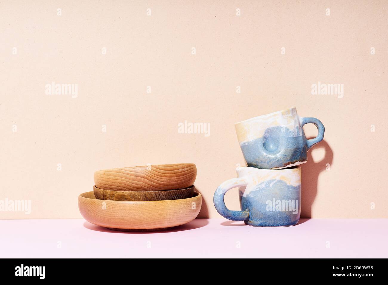 Still life with handmade ceramic cups and wooden bowls on bright studio Stock Photo