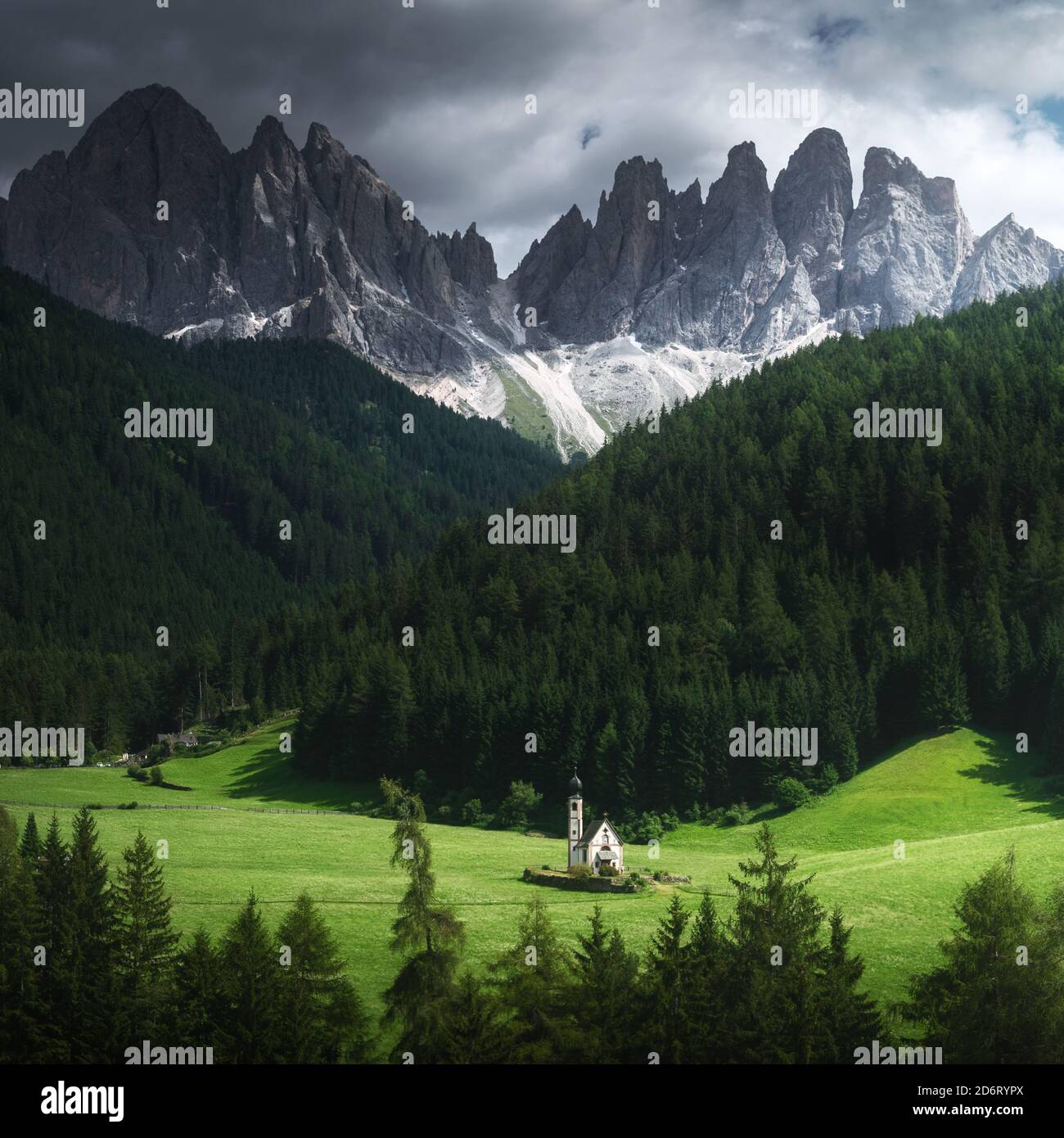 Picturesque view of small aged chantry on green meadow surrounded by trees and mounts under cloudy sky in overcast weather Stock Photo