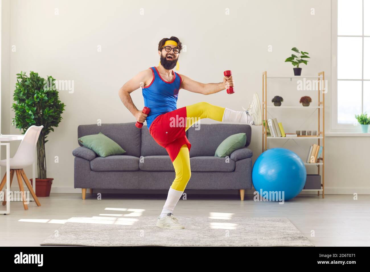 Happy funny young man in retro activewear exercising with dumbbells and laughing Stock Photo