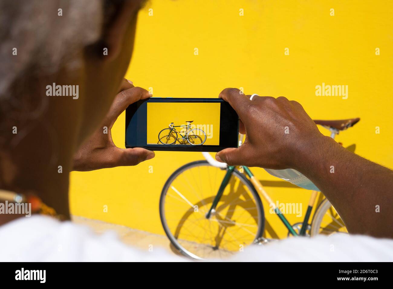 Black man taking a photo of his bike with the phone on a yellow background