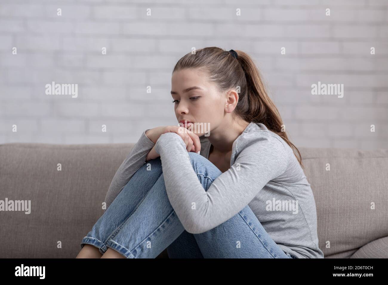Young woman with depression sitting alone on sofa at home Stock Photo