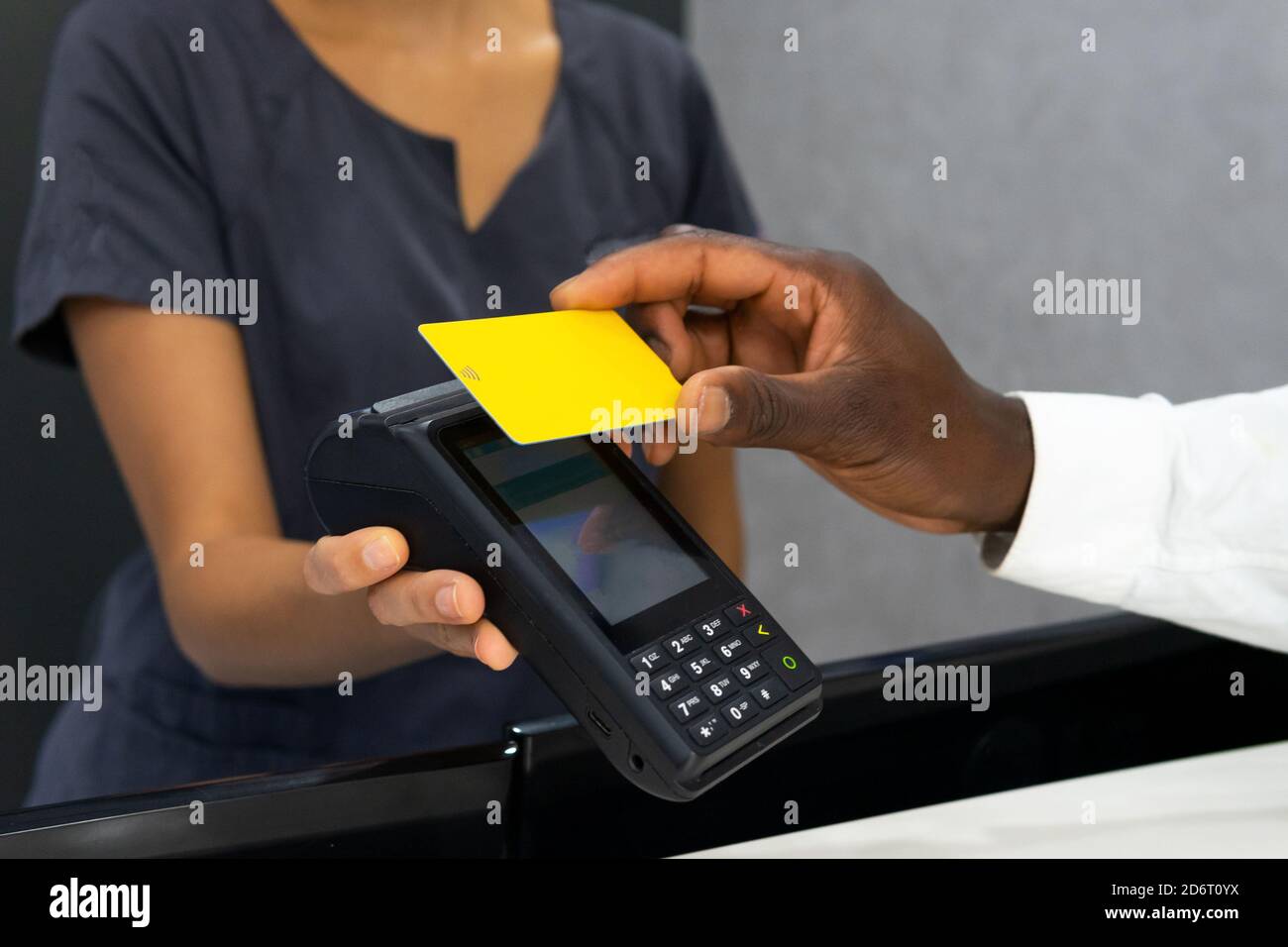 Cropped unrecognizable african American female manager in medical mask receiving payment via POS terminal and plastic card from crop male patient in m Stock Photo