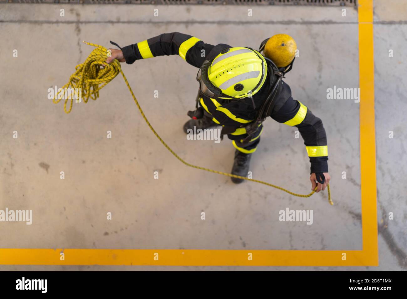 Top view of unrecognizable firefighter in protective hardhat and bright uniform standing on cement floor with rope during routine practices at work Stock Photo