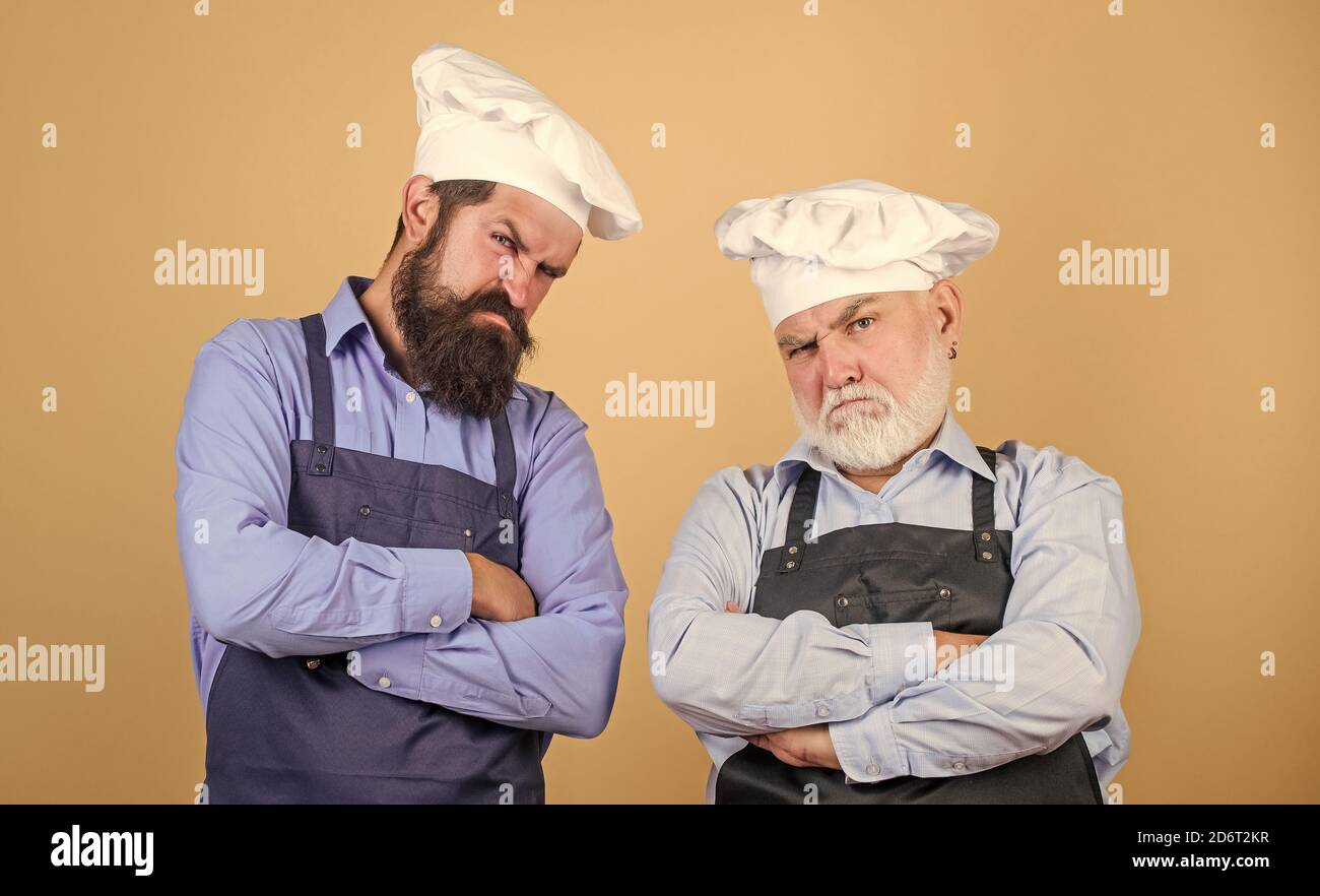 Culinary battle. Mature bearded men professional restaurant cooks competitors. Culinary show. Chef men wear aprons. Father and son culinary hobby. Cafe workers. Culinary industry. Restaurant staff. Stock Photo
