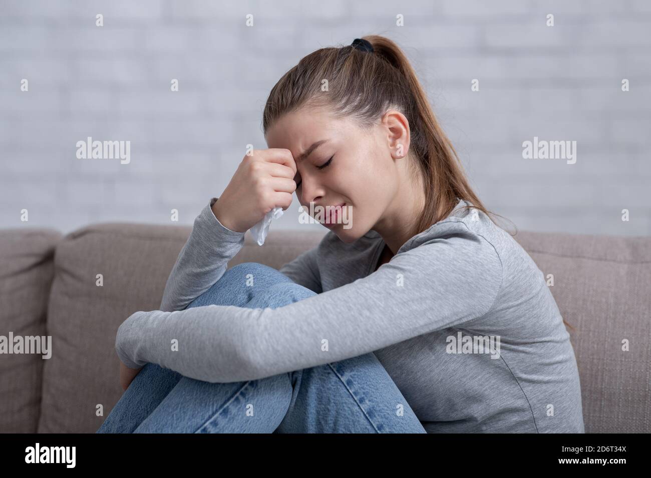 Lonely millennial woman feeling hopeless or desperate, crying on sofa at home Stock Photo