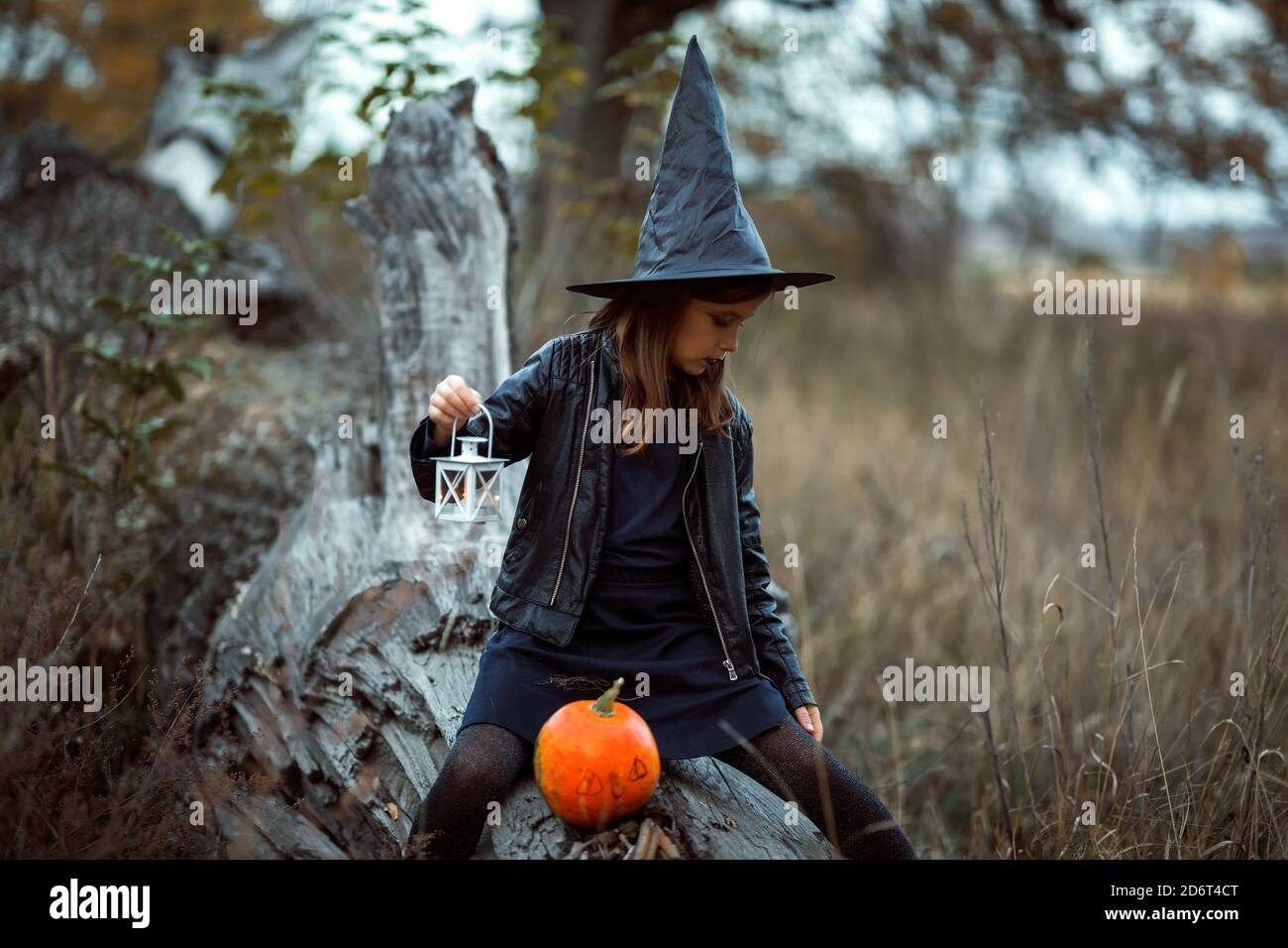 Cute teen girl in a Halloween costume outside holding lights and an orange pumpkin in her hands. Stock Photo