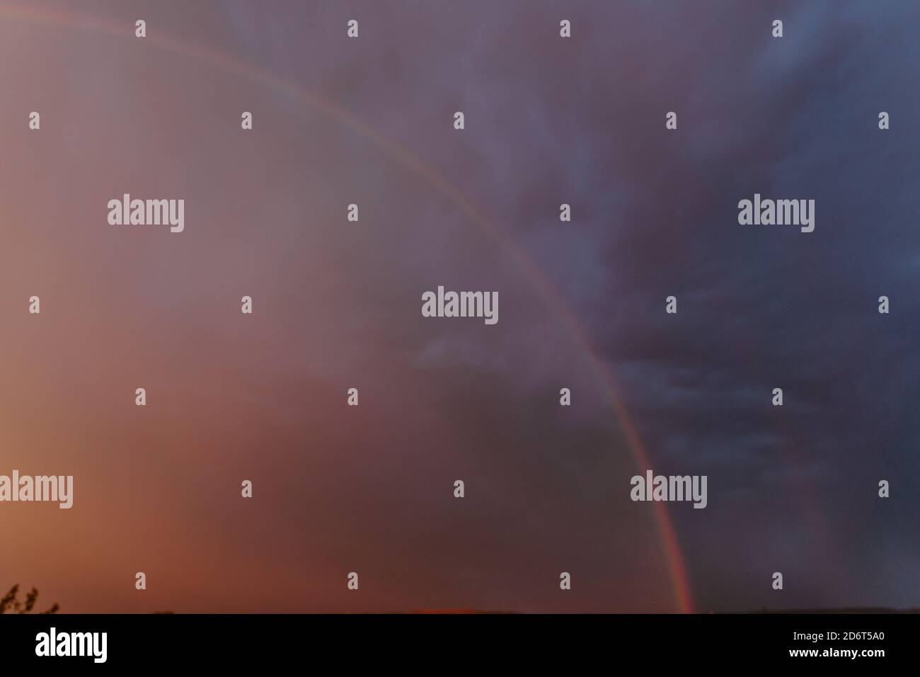 Scenery of vibrant rainbow shining on dark dramatic sky covered with thick heavy clouds in evening Stock Photo