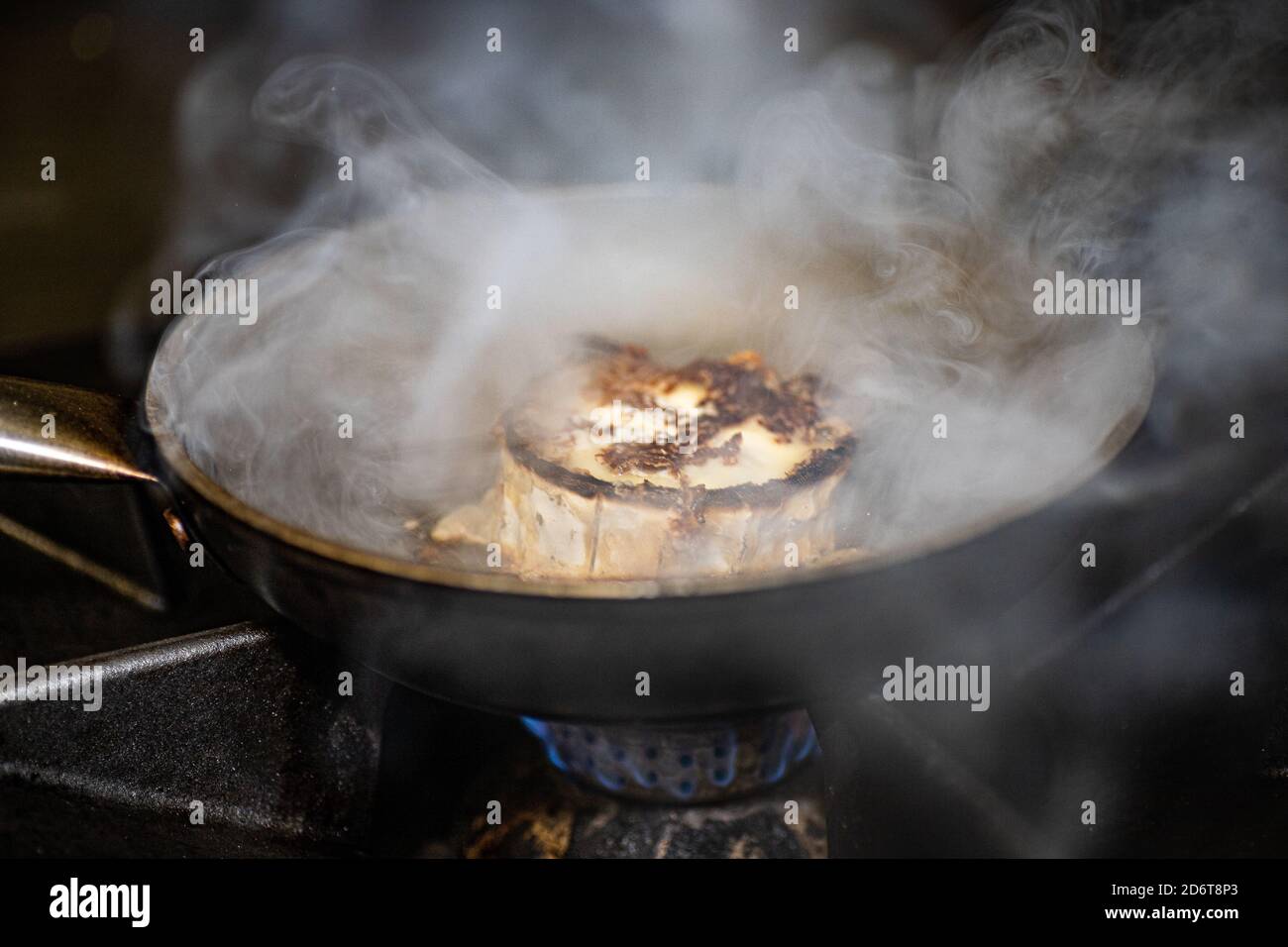 Steaming seared cheese being prepared in iron frying pan on gas stove in restaurant kitchen Stock Photo