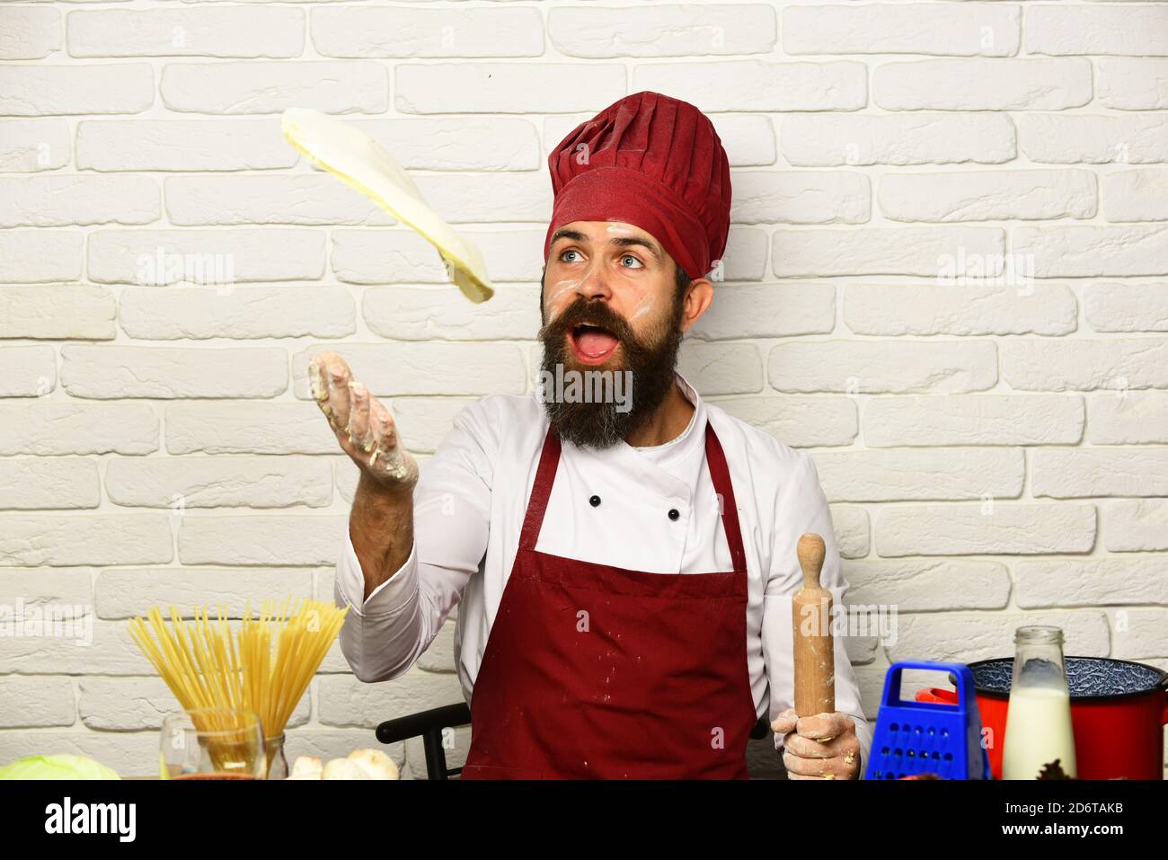 Cook with excited face in burgundy uniform sits by table with