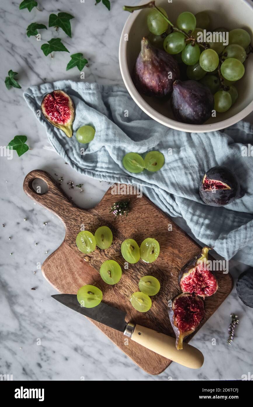 Top view of delicious grapes and figs arranged on marble table with cutting board and kitchen towel Stock Photo