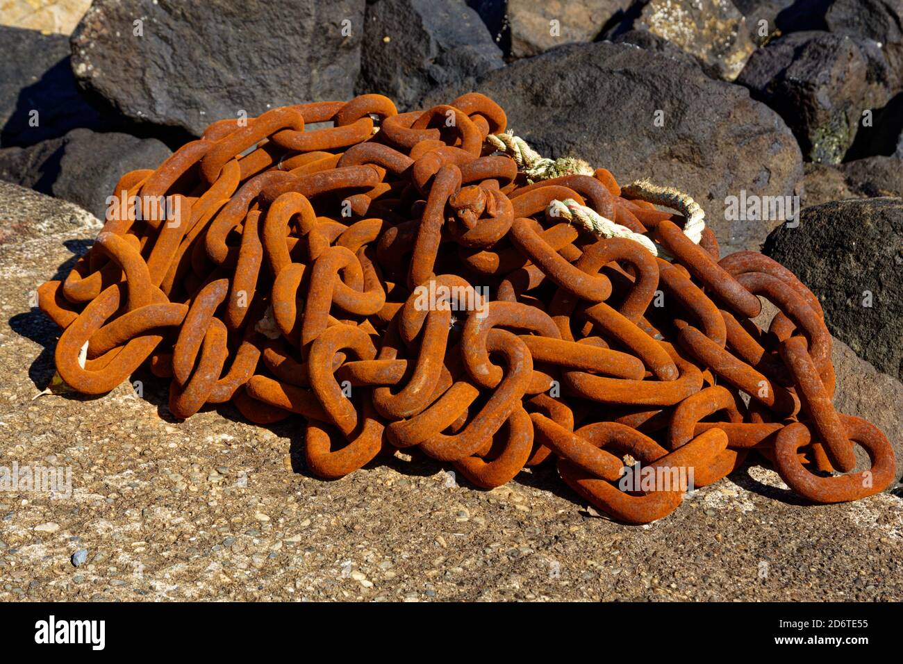 A piled up length of rusty chain glows in the afternoon sun on the concrete slipway by the marina in Ledaig at Tobermory Stock Photo