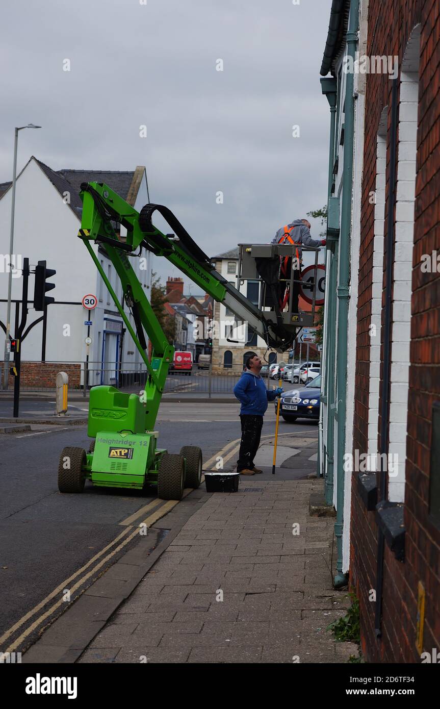 Workers using a Nifty Height Rider 12 boom lift to reach a window on the High street. Stock Photo