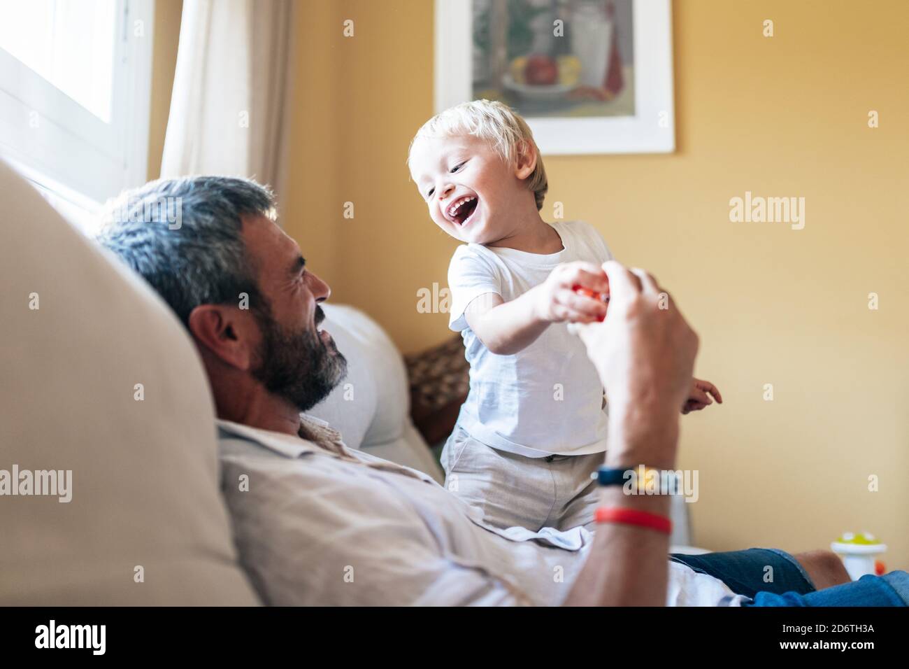 Cheerful man in casual clothing playing with happy blond haired boy in bright room Stock Photo