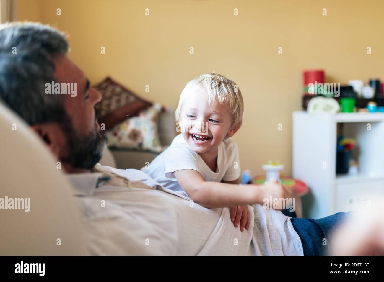 Cheerful man in casual clothing playing with happy blond haired boy in bright room Stock Photo