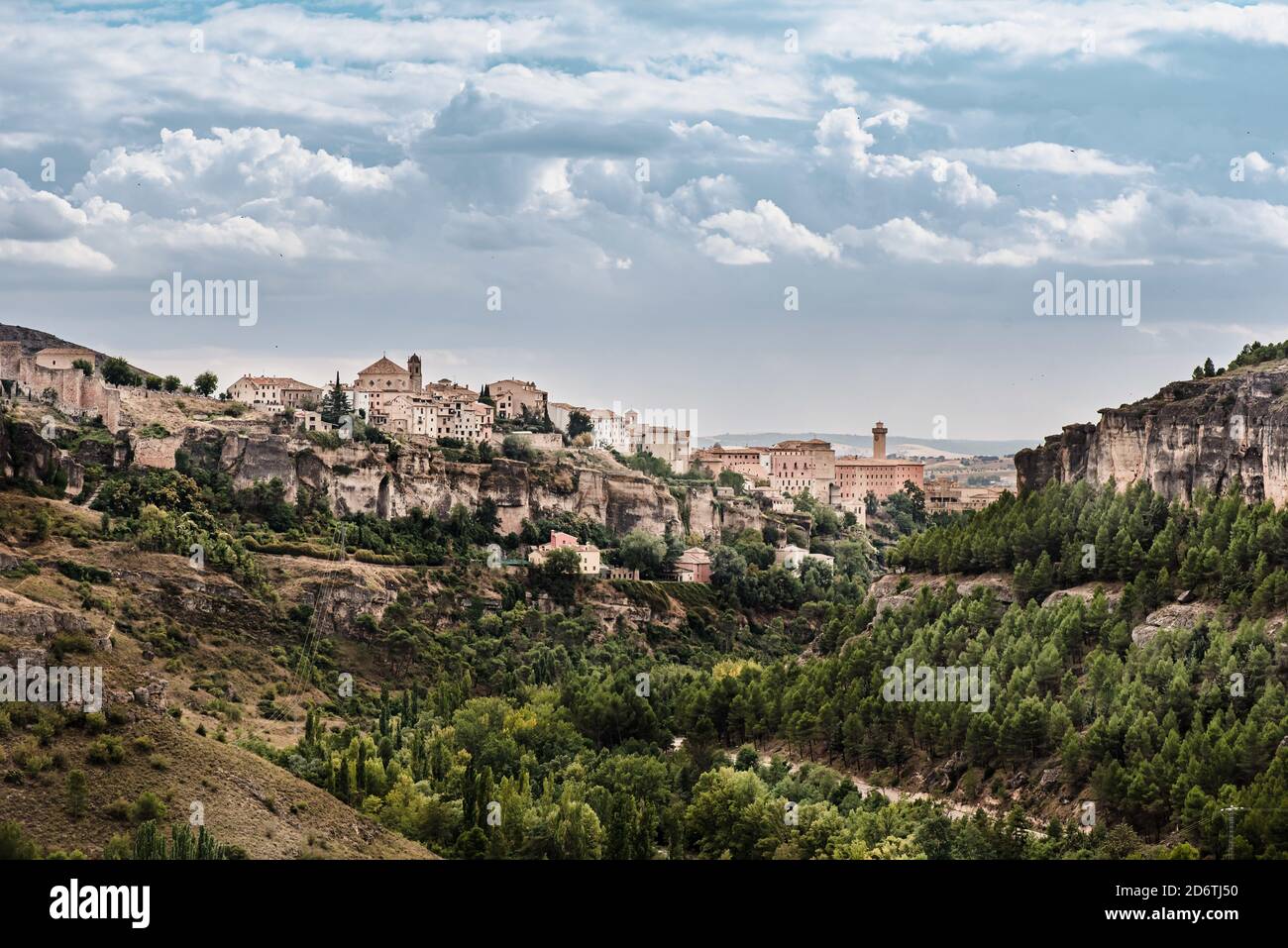 Scenic view of medieval town Cuenca with old stone houses located on hills covered with green trees under blue cloudy sky in summer day in Spain Stock Photo