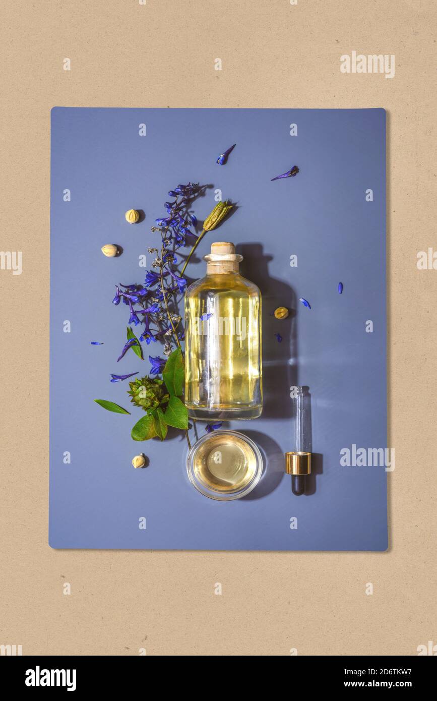 Bottle with natural cosmetic aroma oil and pipette on blue background in flowers Stock Photo