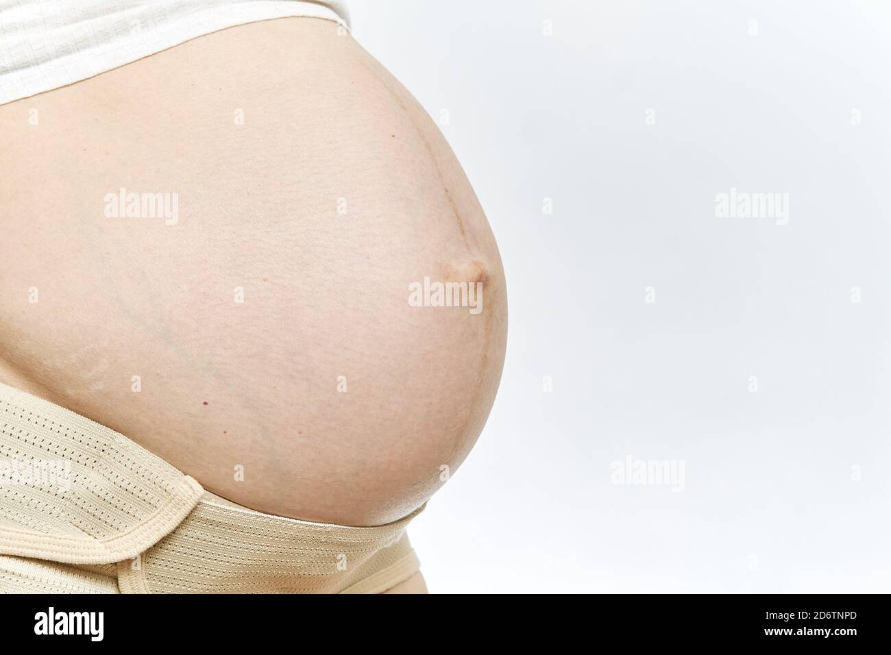 Pregnant woman's belly faceless close-up isolated. Maternity Belt Pregnancy Abdomen Support Abdominal Binde. side view and copy space. Stock Photo