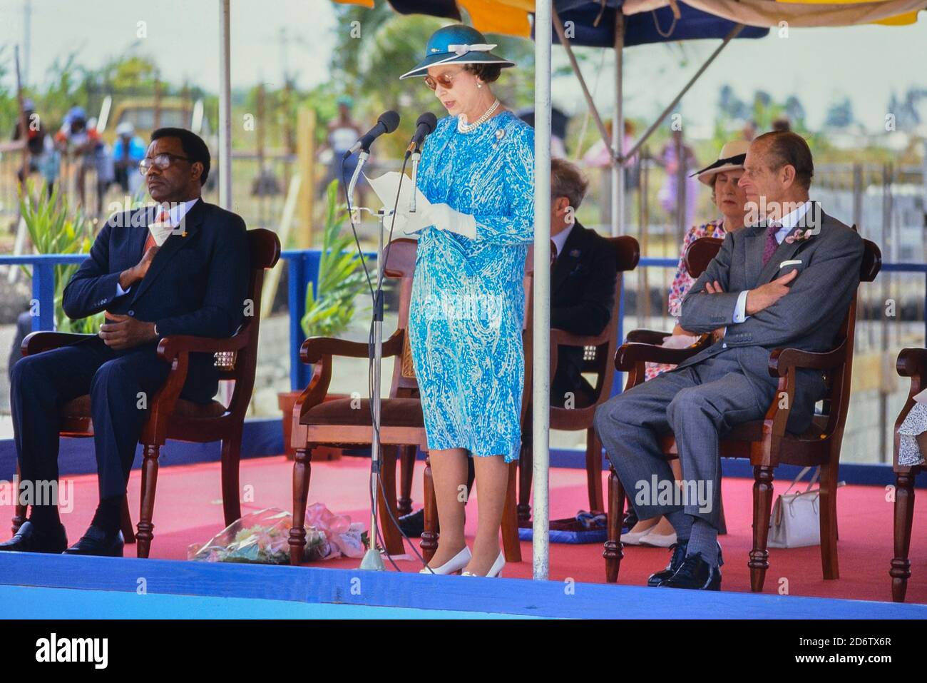 Queen Elizabeth II giving a speech accompanied by Prince Philip, Duke of Edinburgh to a visit to Queen's College to officiate at a stone laying ceremony for the new school building. Barbados, Caribbean. 1989 Stock Photo
