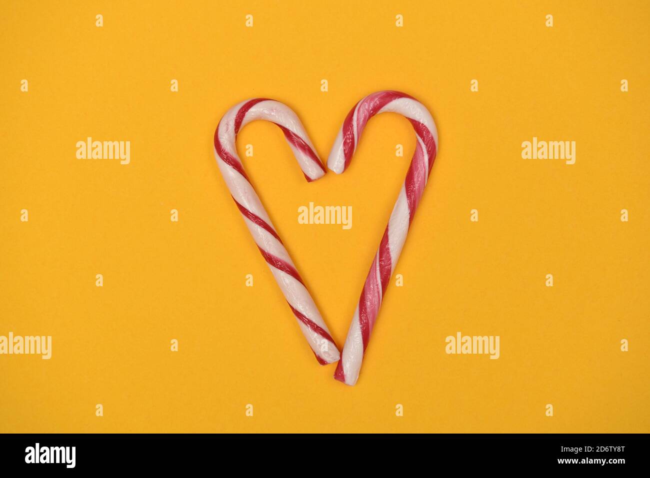 Candy canes shaped as a heart on a yellow background Stock Photo