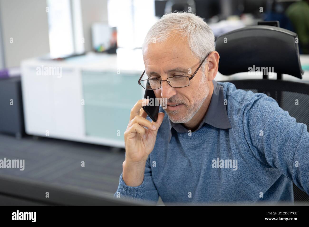 Senior businessman talking on smartphone while sitting on his desk at modern office Stock Photo