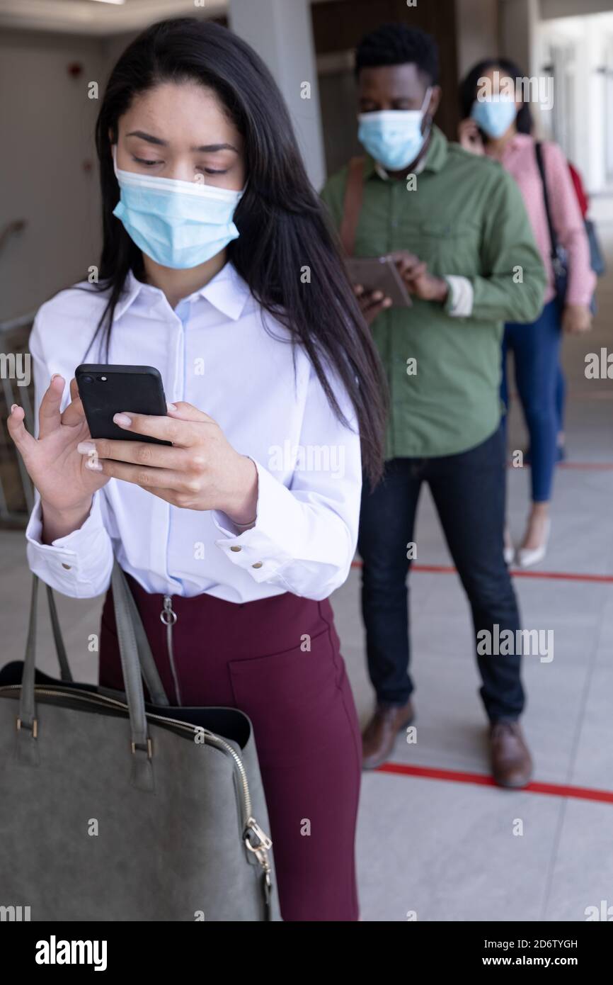 Businesswoman wearing face mask using smartphone while standing in queue Stock Photo