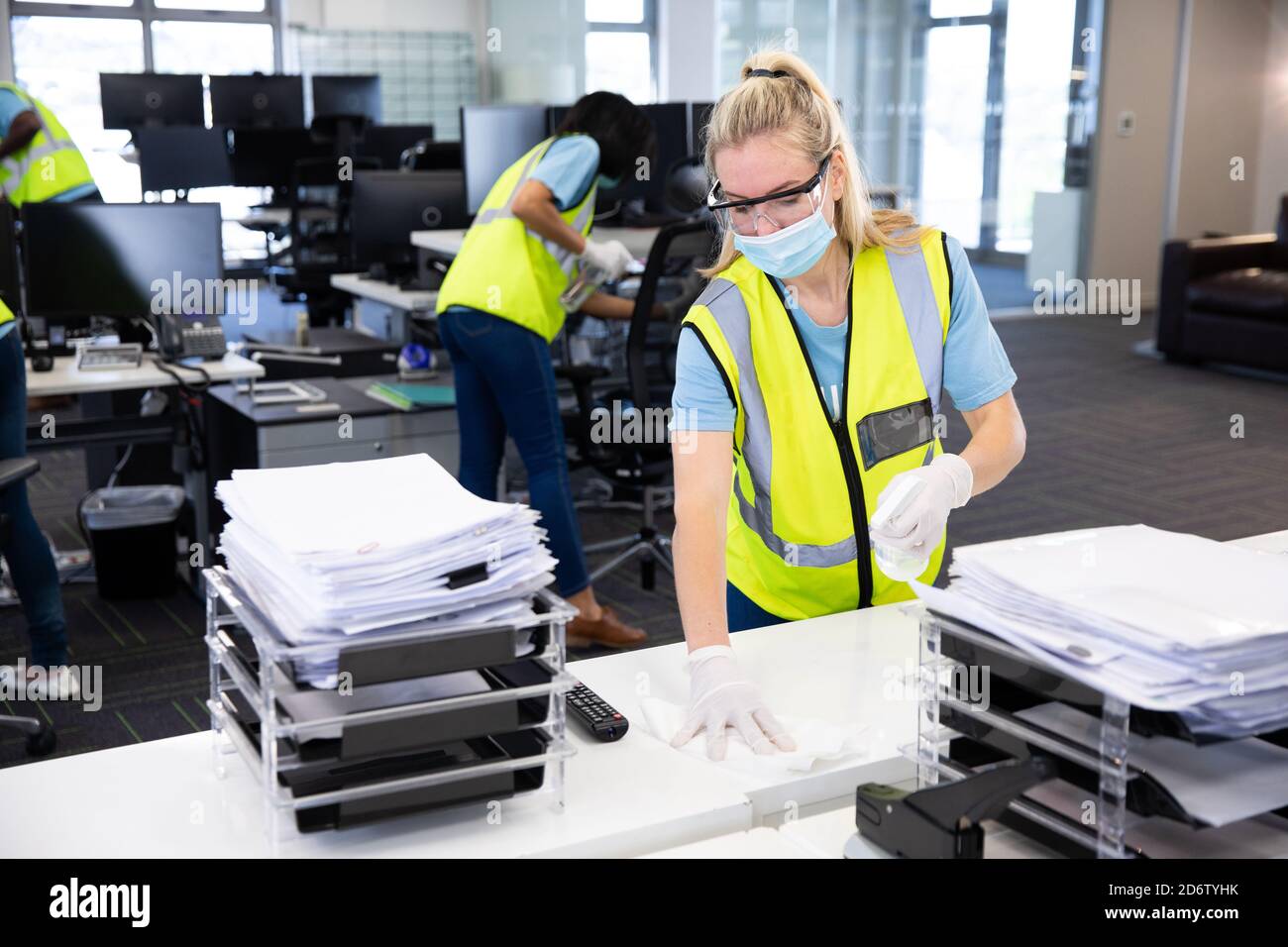 Woman wearing hi vis vest and face mask cleaning the office using disinfectant Stock Photo