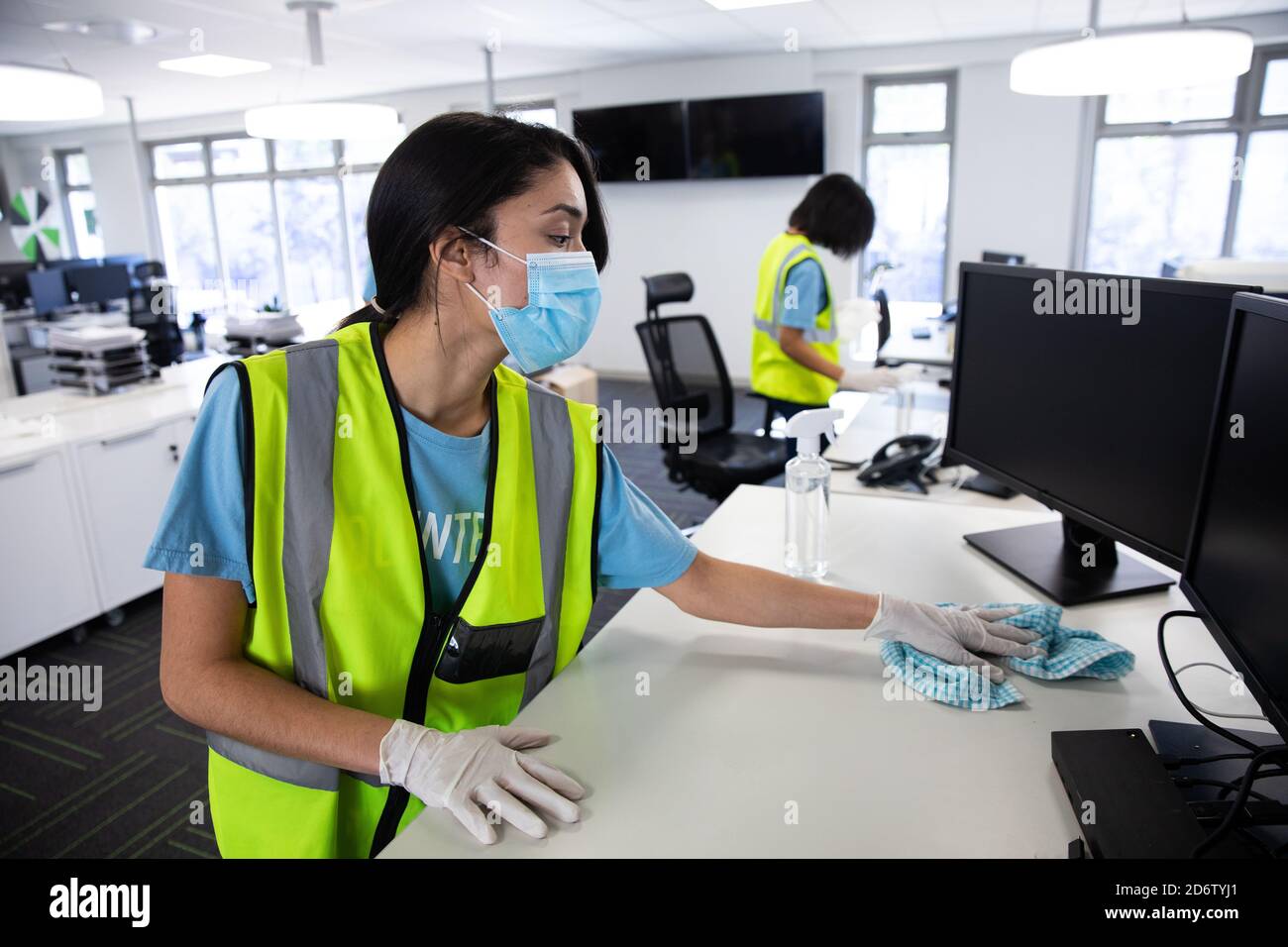 Woman wearing hi vis vest and face mask cleaning the office using disinfectant Stock Photo