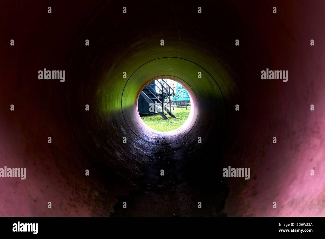 View through a dark tube with red coating to a black metal staircase Stock Photo