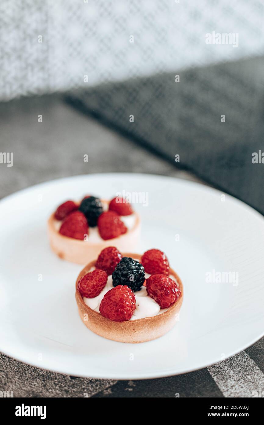 Delicious tartlets or cake with mixed berry on white plate in the kitchen. Summer pastry desserts. Vertical photo orientation Stock Photo