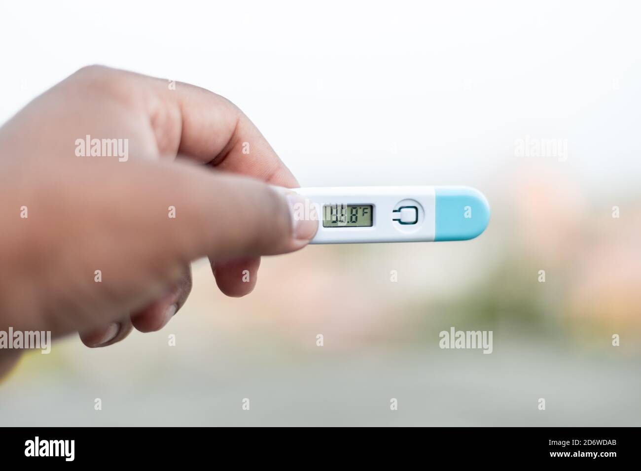 Sick man holds digital thermometer with body temperature reading in Fahrenheit up close to the camera. Stock Photo
