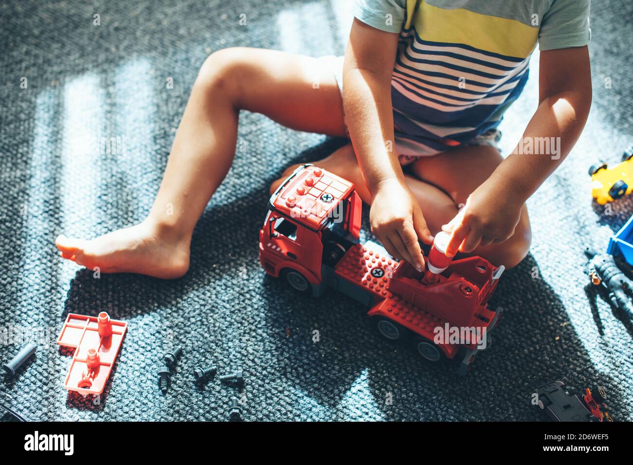 Upper view photo of a boy sitting on the floor and building a car from constructor Stock Photo