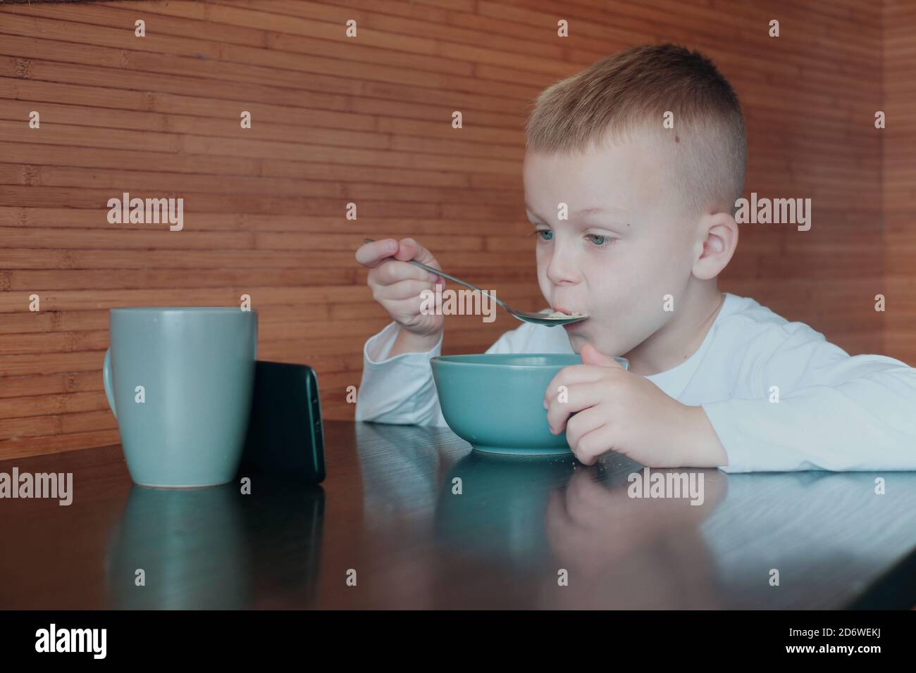The child eats food and looks at the gadget.put the phone on the mug