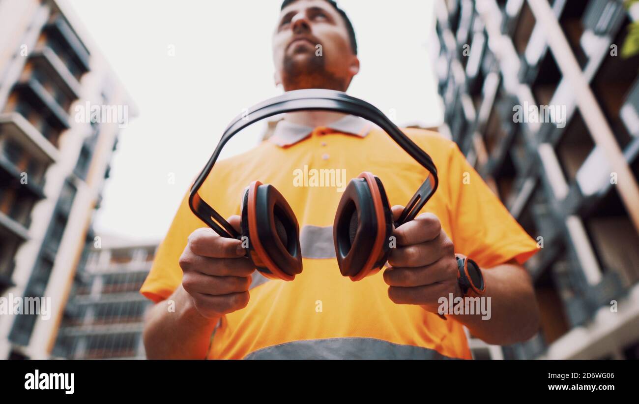 Builder covers his ears, ear muff to protect workers ears. Construction