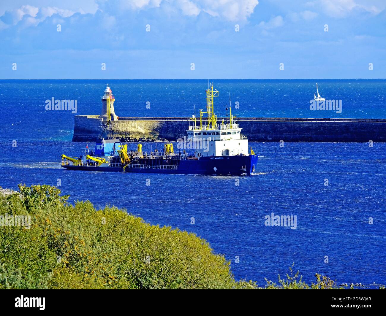 UKD Marlin dredging a channel in the mouth of the river Tyne with blue sky and sailing boat Stock Photo
