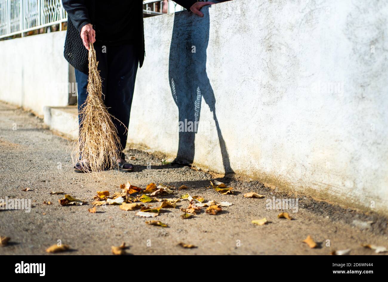 Senior woman cleaning fallen autumn leaves on the street Stock Photo